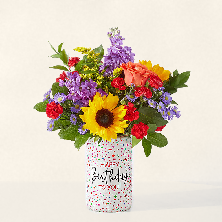 Celebrating You birthday bouquet with sunflowers, orange roses and purple flowers in a Happy Birthday confetti vase, hand-arranged by Baldwin Park florist