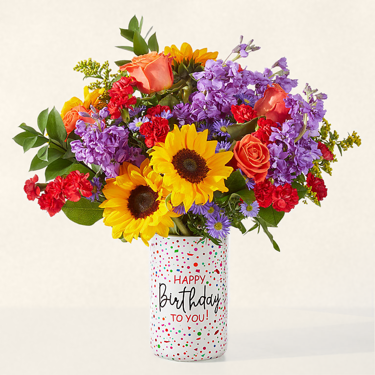 Colorful birthday bouquet with fresh sunflowers, roses and purple blooms in a festive birthday vase