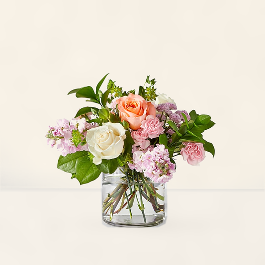 French Market bouquet with pastel peach, cream and blush roses with purple accents in a clear glass vase, hand-arranged by Baldwin Park florist