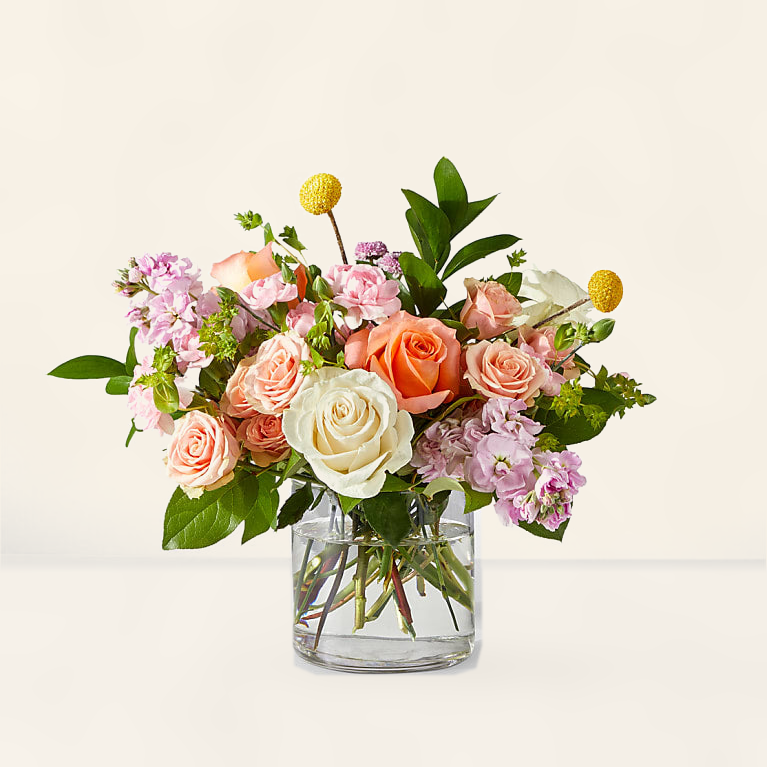 Elegant pastel rose bouquet — soft peach and cream roses with fresh greenery in glass vase