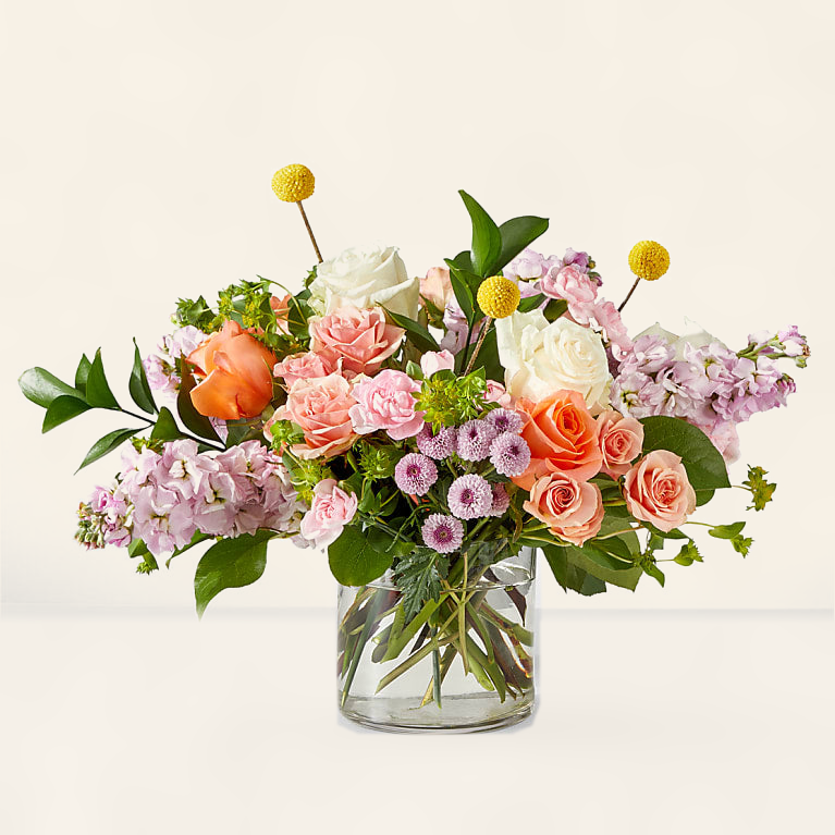 Parisian-style pastel flower arrangement with blush roses and purple blooms in clear vase