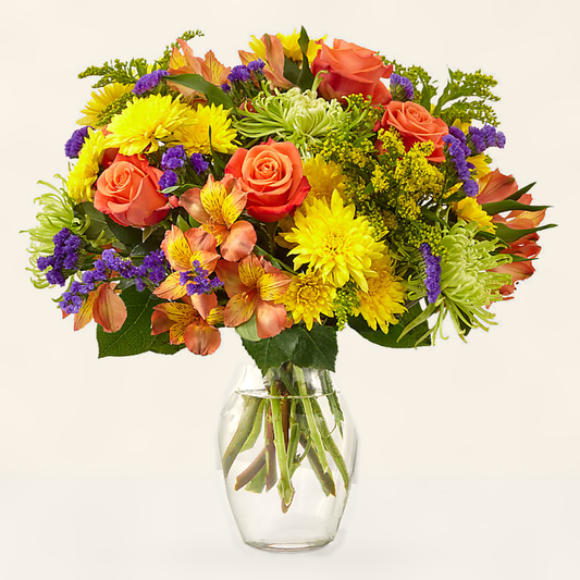 Marmalade Skies bouquet with vibrant orange roses, yellow blooms and purple accents in a clear glass vase, hand-arranged by Baldwin Park florist