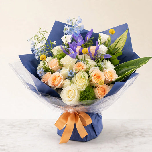 Blue Horizon Graduation Bouquet — white and peach roses with blue iris and delphinium hand-wrapped in navy paper, by LaLa Florist in Baldwin Park